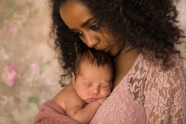 Mother in pink lace dress holding her 1 week old little baby