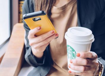 woman holding a cell phone in one hand and a grande starbucks beverage in the order