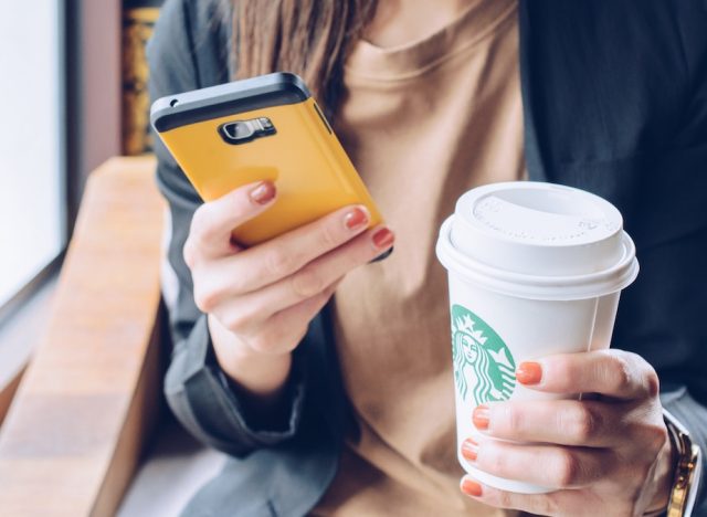 woman holding a cell phone in one hand and a grande starbucks beverage in the order