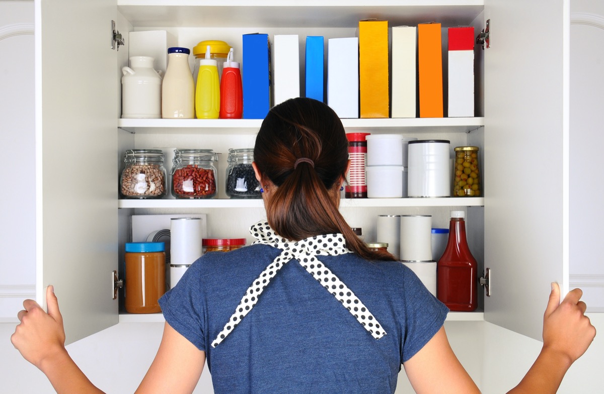 A woman seen from behind opening the doors to a fully stocked pantry. The cupboard is filled with various food stuff and groceries all with blank labels