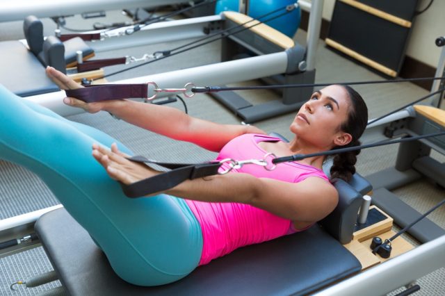 Femeie brunetă Pilates Reformer Exerciții de antrenament la sala de gimnastică interioară