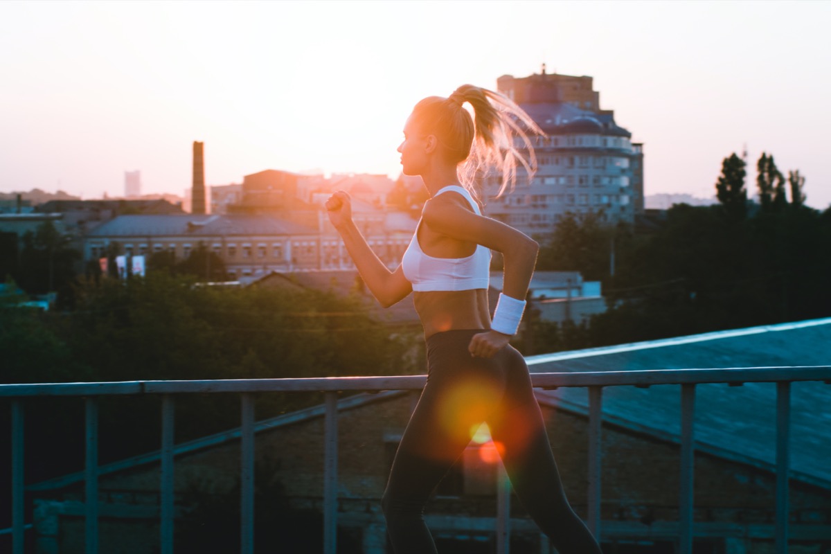 woman in sports wear jogging against industrial city view with sunrise