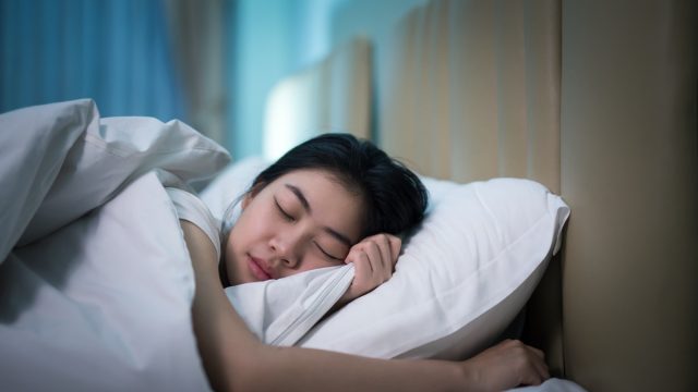 Asian woman sleeping in a bed in a dark bedroom