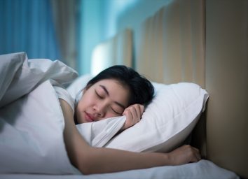 Asian woman sleeping in a bed in a dark bedroom