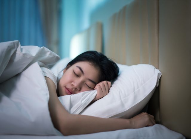 Asian woman sleeping in a bed in a dark bedroom