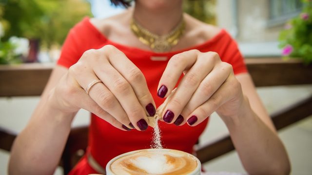 Female hand poured sugar into coffee, cappuccino