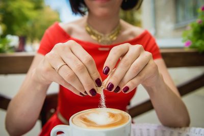 Female hand poured sugar into coffee, cappuccino