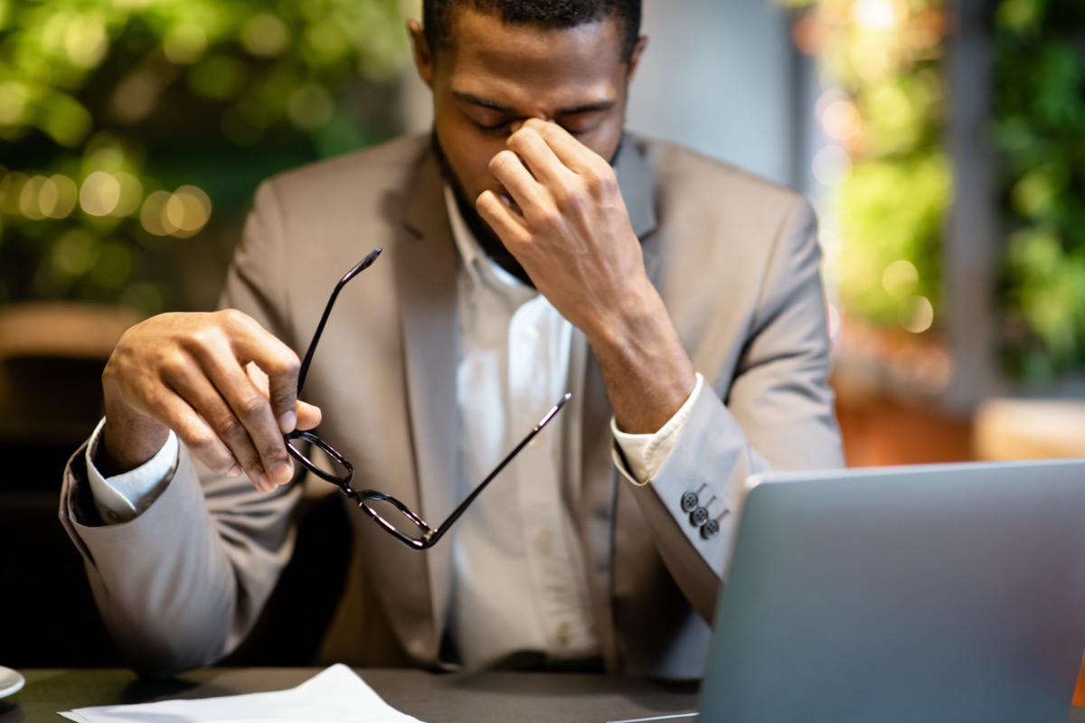 Tired Of Work. Fatigued black businessman taking off glasses, massaging nose, working in cafe