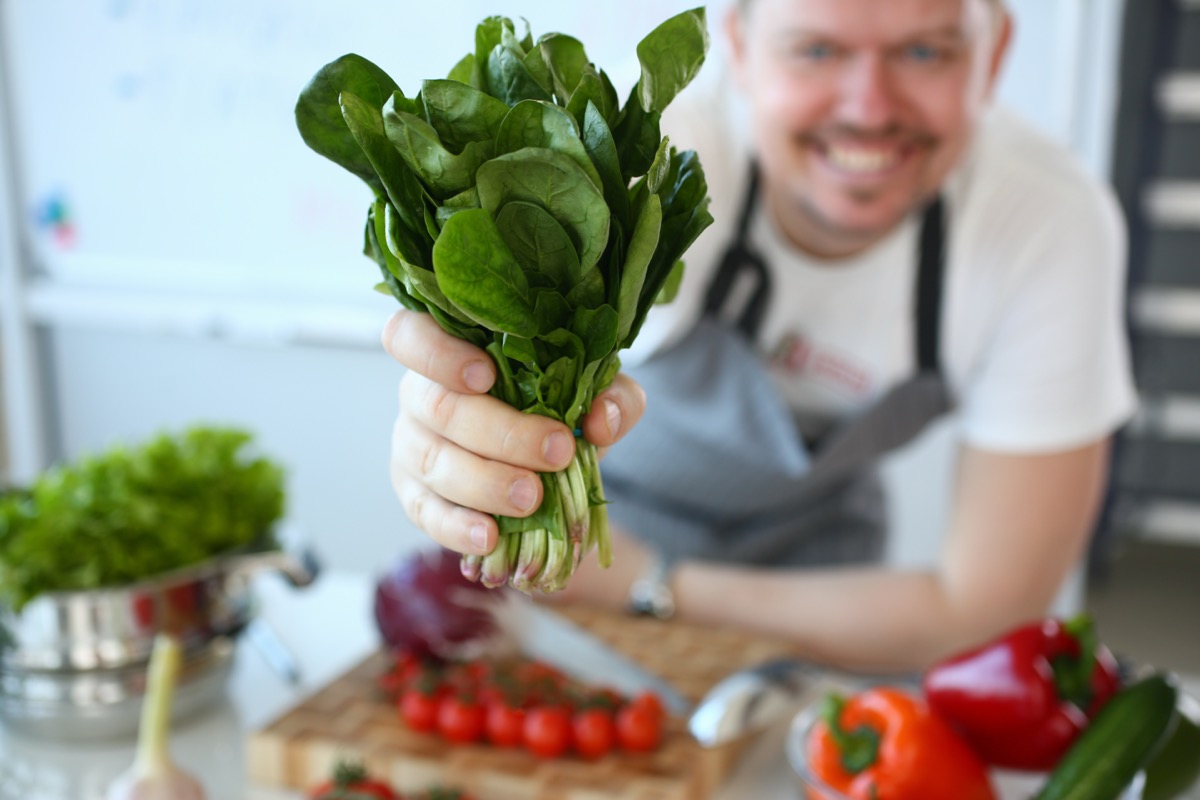 Man hold useful bunch of spinach in hand closeup on kitchen background