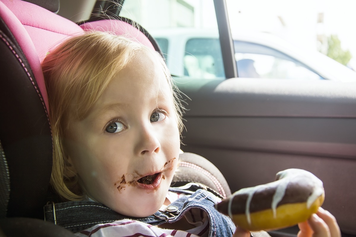 little girl eating chocolate donuts in car