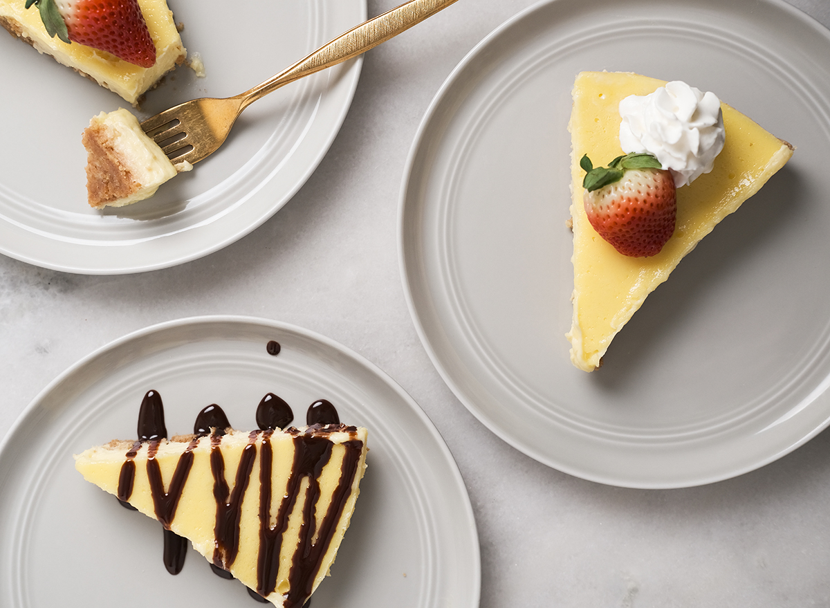 slices of cheesecake with strawberries whipped cream and chocolate sauce on grey plates