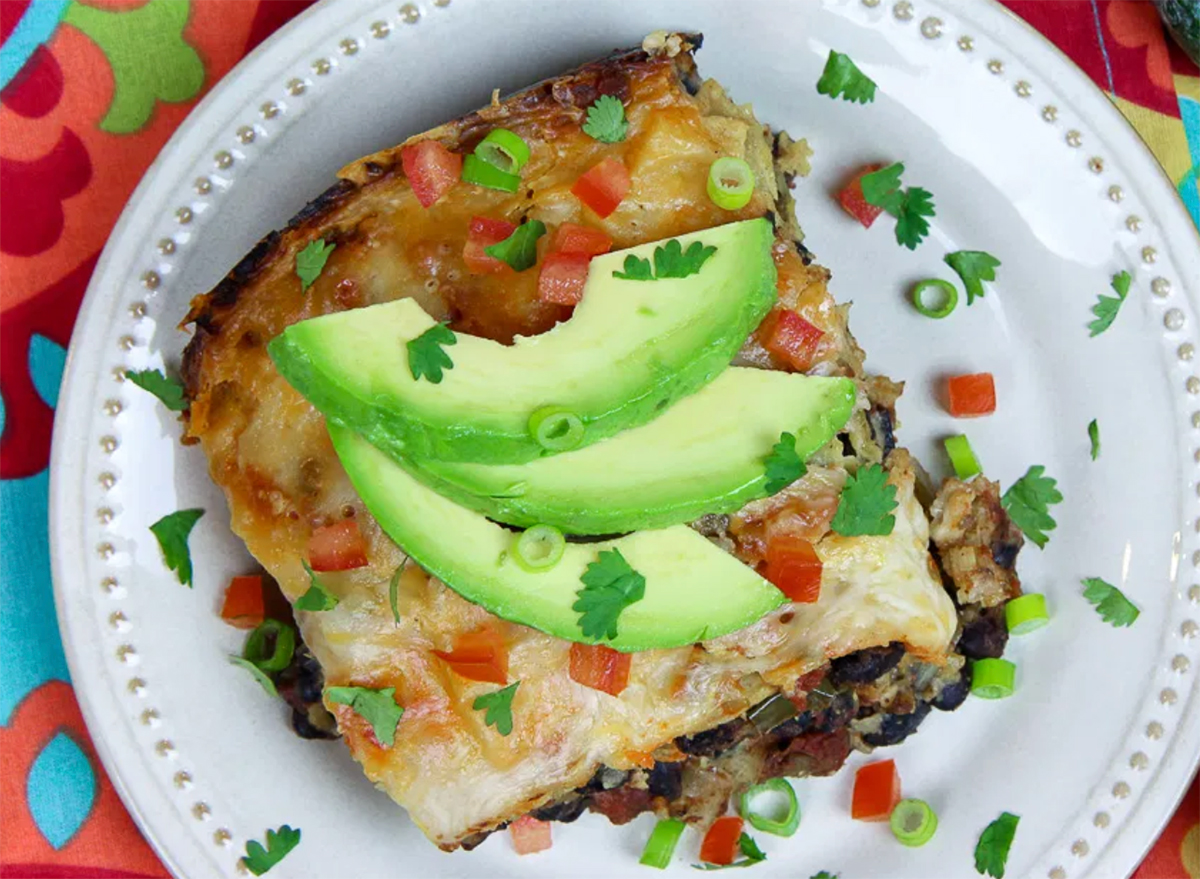 vegetarian enchilada topped with avocado slices on white plate