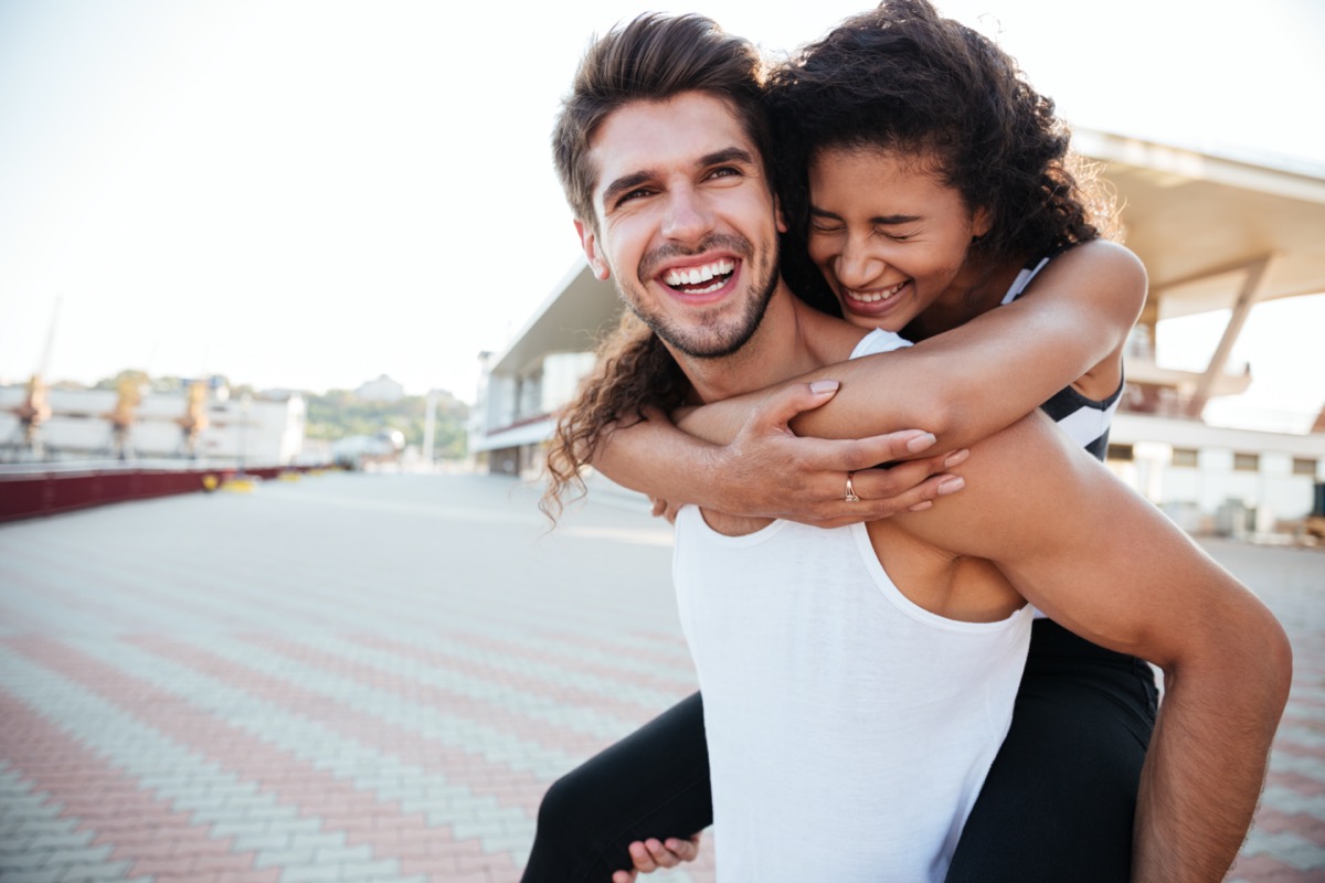 Smiling young man carrying woman on his back and laughing outdoors
