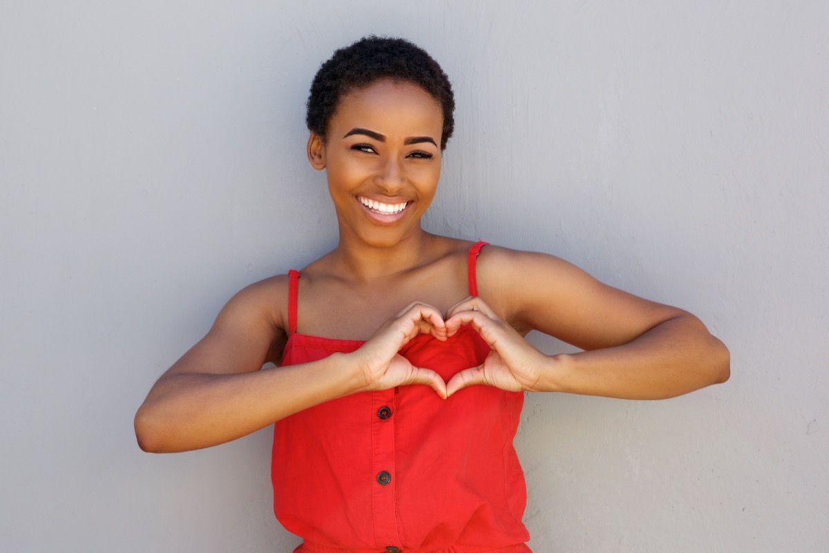 Smiling woman with heart shape hand sign.