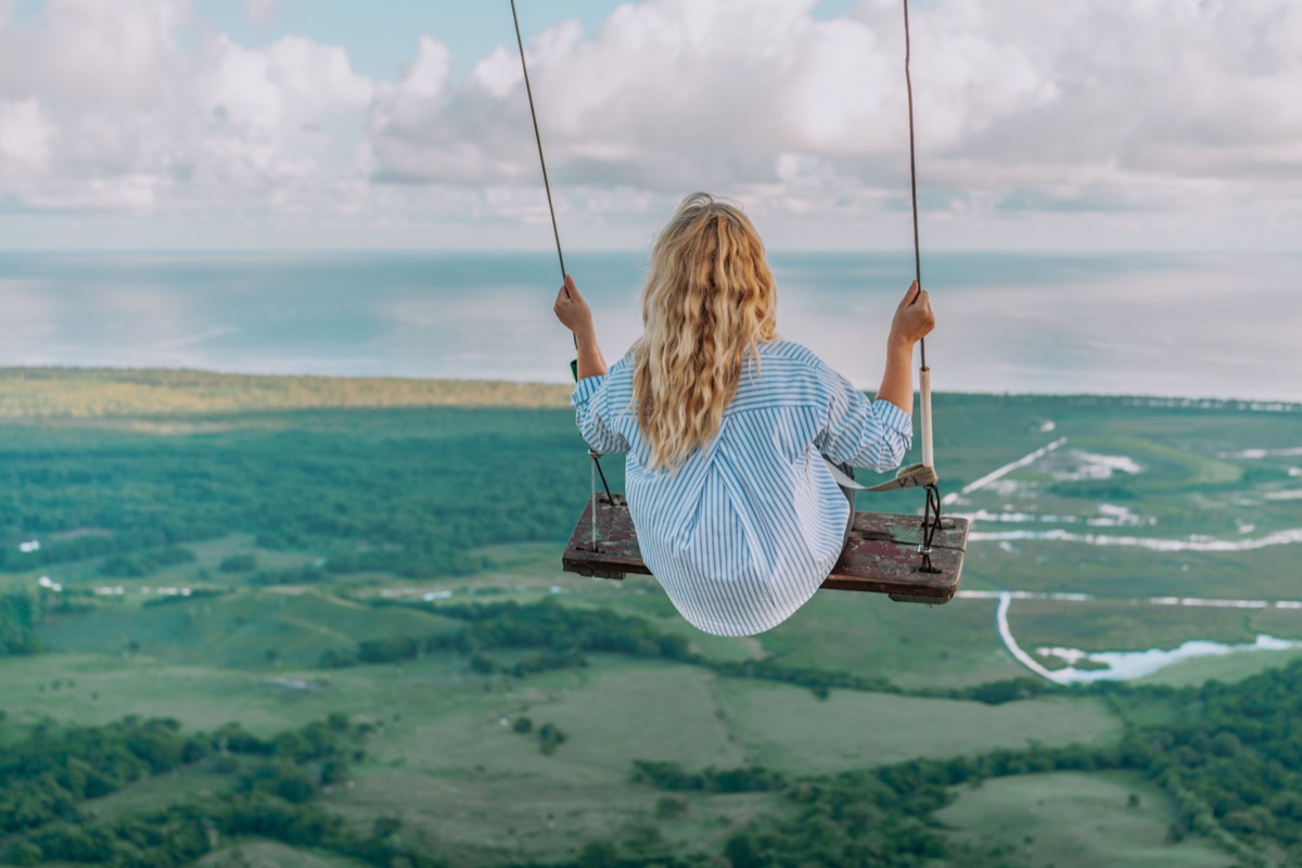 Beautiful view of young woman swing on the top of the mountain