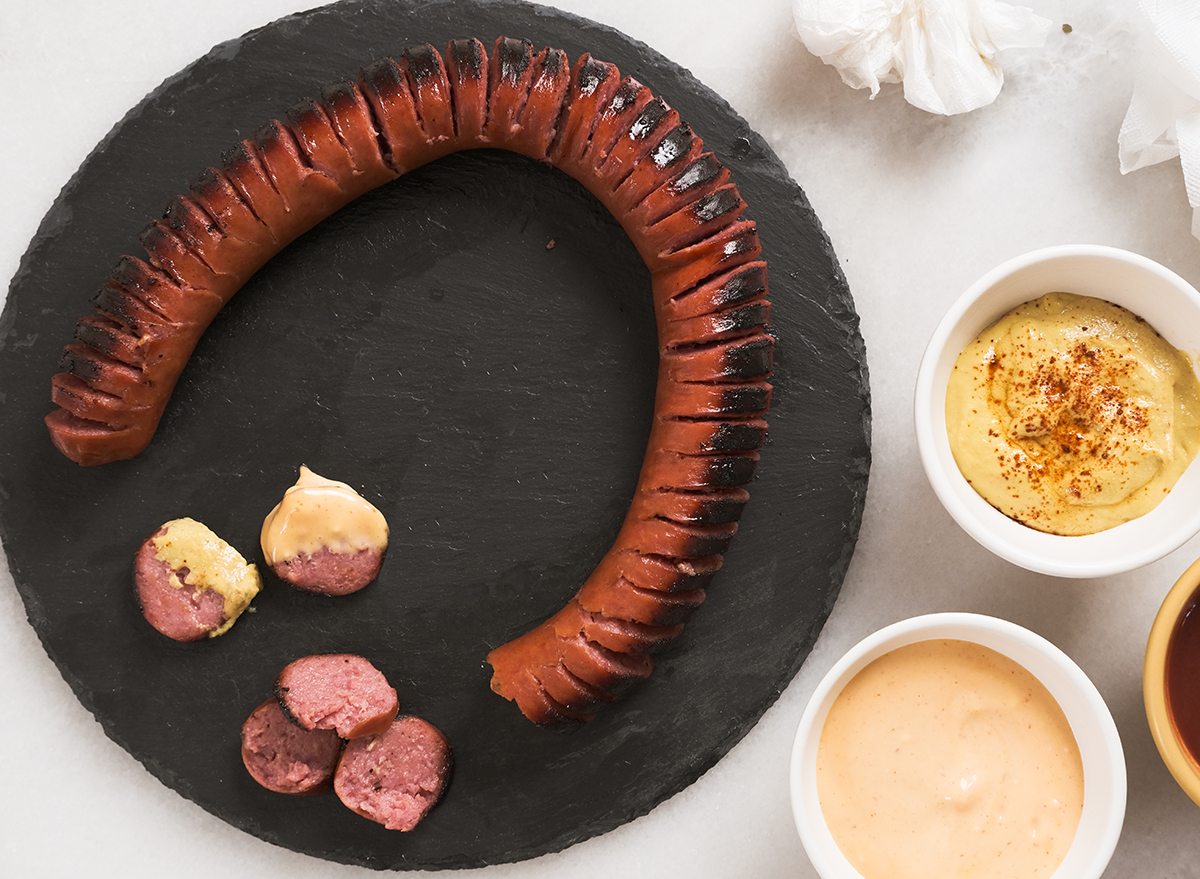 hasselback kielbasa on a cutting board with three dipping sauces