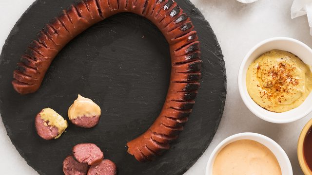 hasselback kielbasa on a cutting board with three dipping sauces