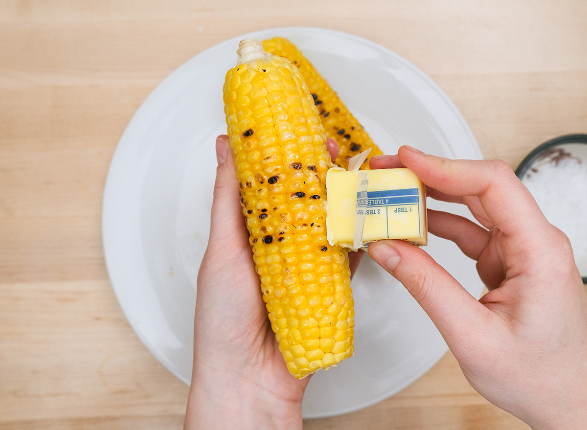 rubbing butter on a cooked corn on the cob