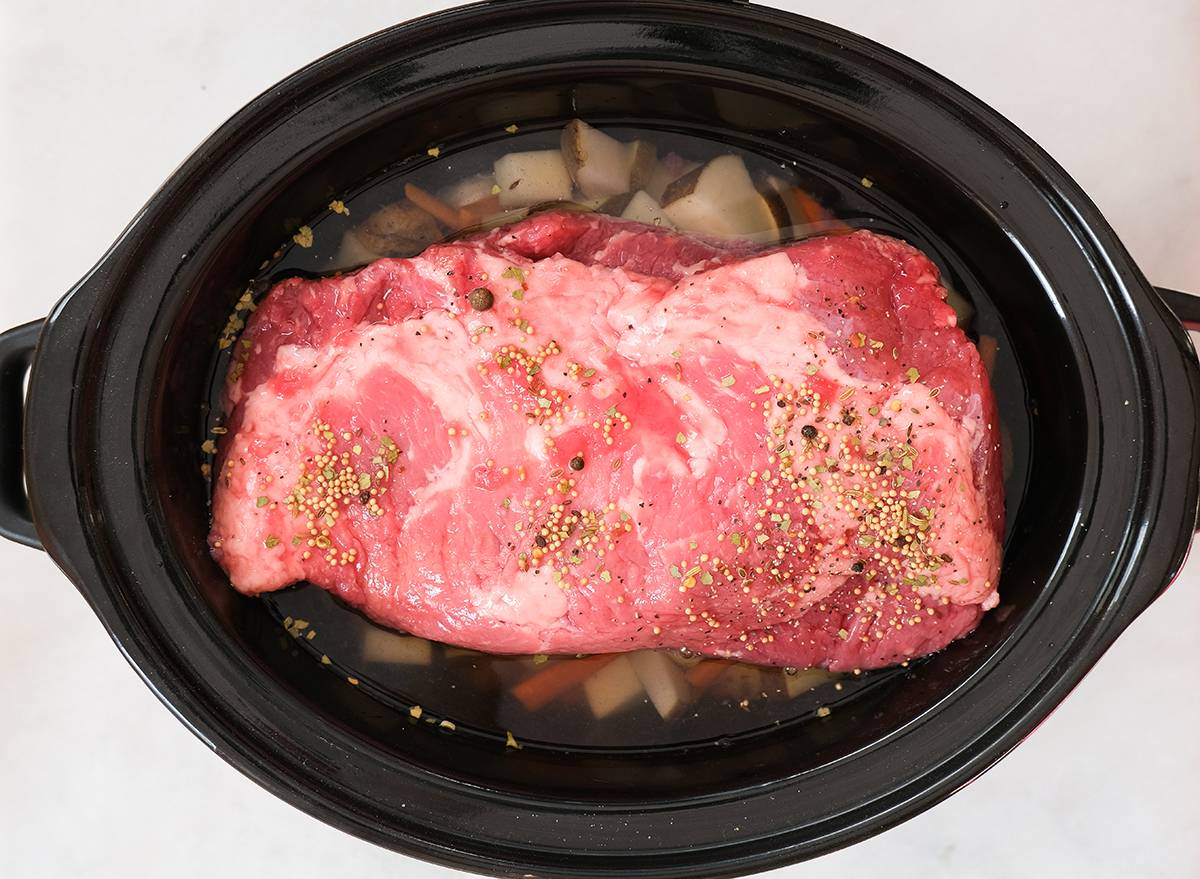 adding water to a slow cooker with seasoned corned beef