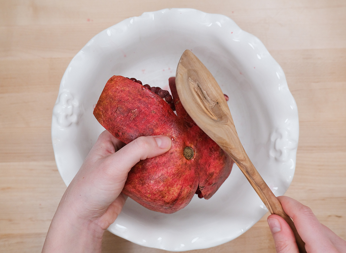 deseeding pomegranate with a wooden spoon