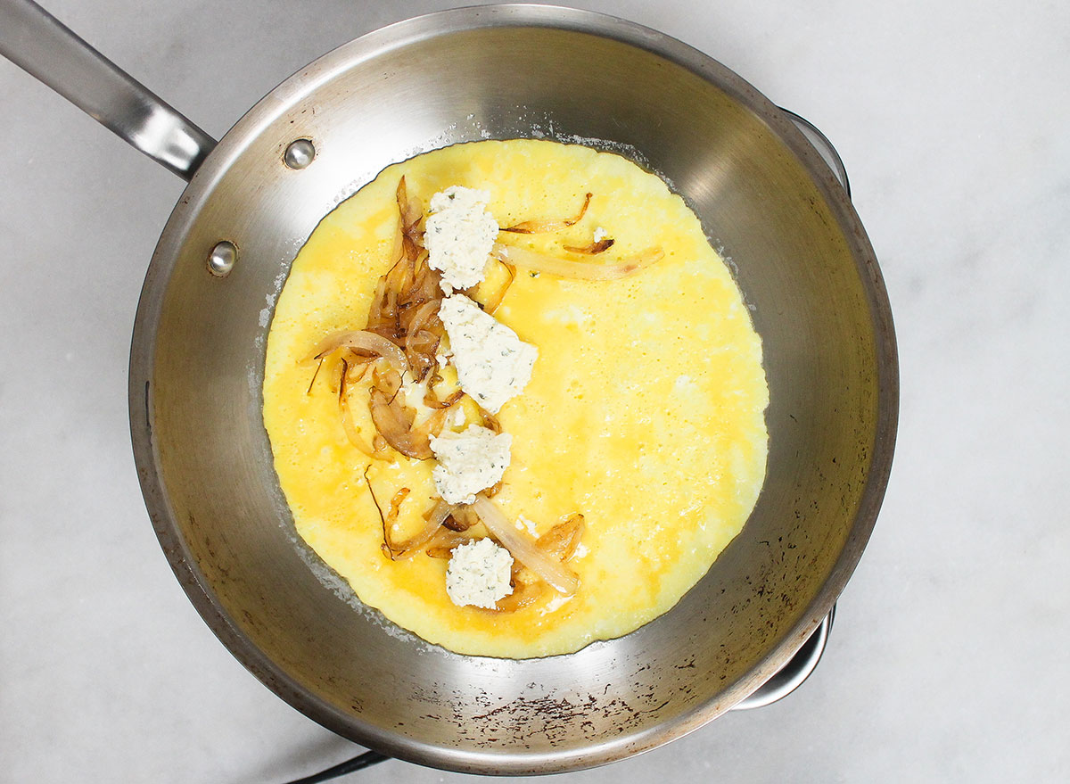 adding boursin cheese and caramelized onions into a pan with egg mixture