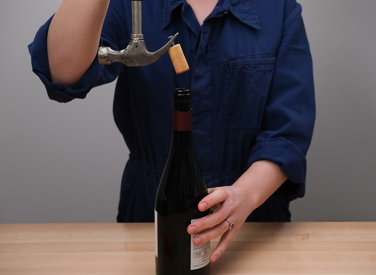 pulling a cork out of a bottle of wine using a nail and a hammer