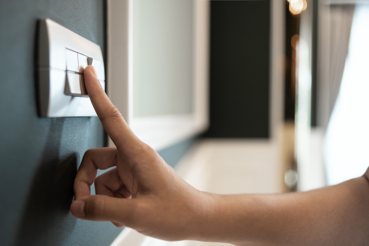 Asian female right hand is turning on or off on grey light switch