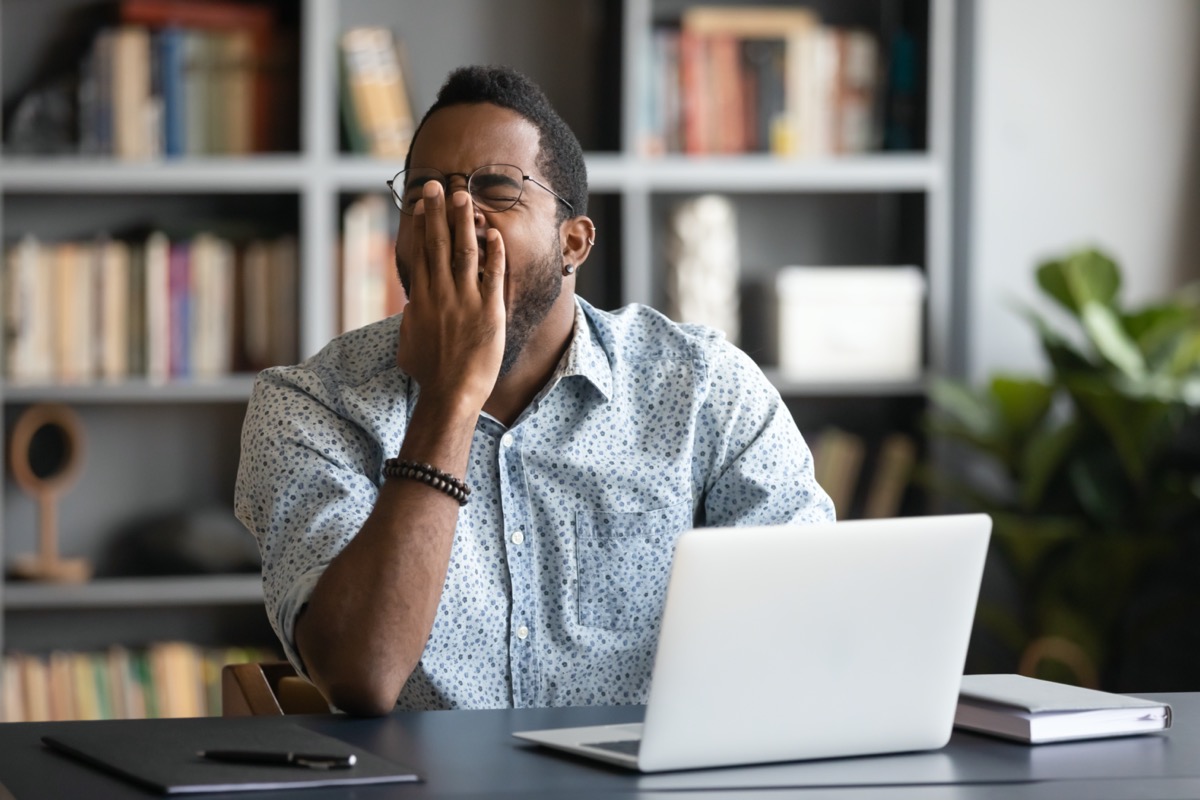 Tired african American male worker or student sit at desk sigh yawn feeling stressed or fatigue overwork in office