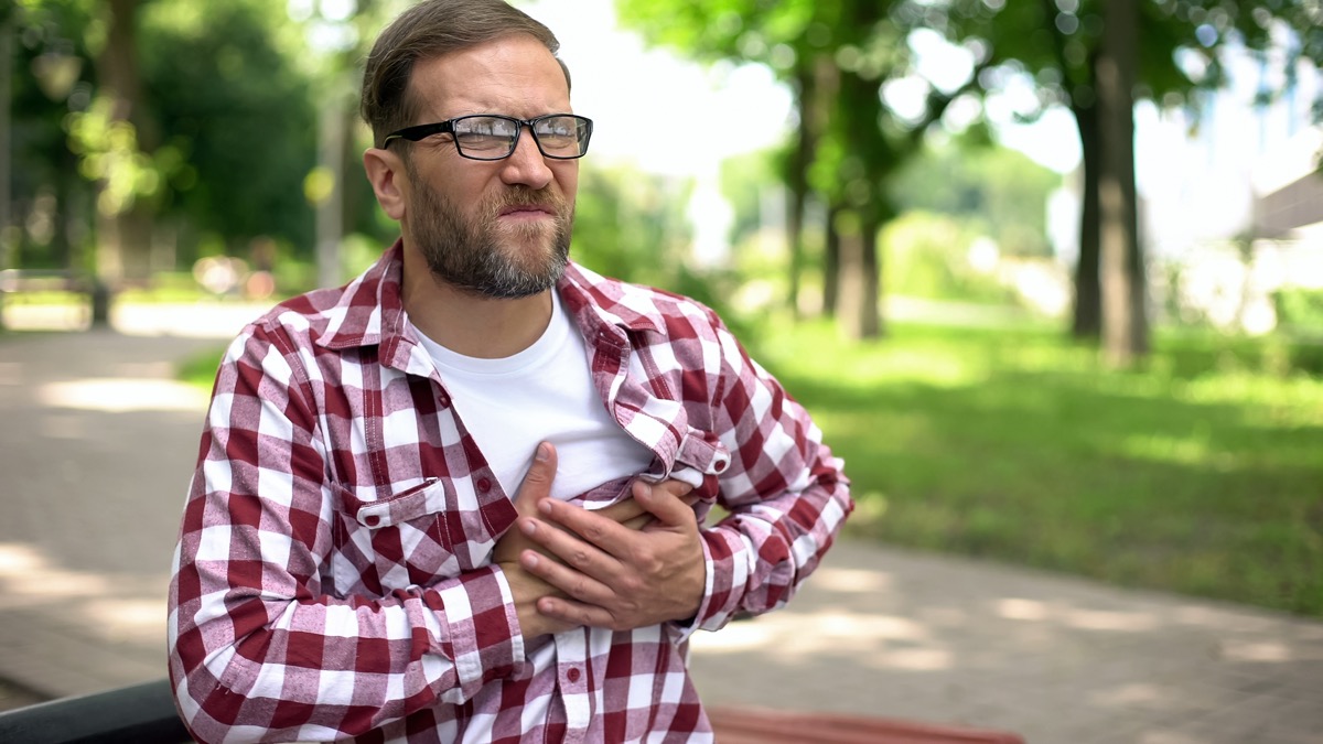 Man suffering chest pain, sitting outdoors, heart arrhythmia, ischemic disease