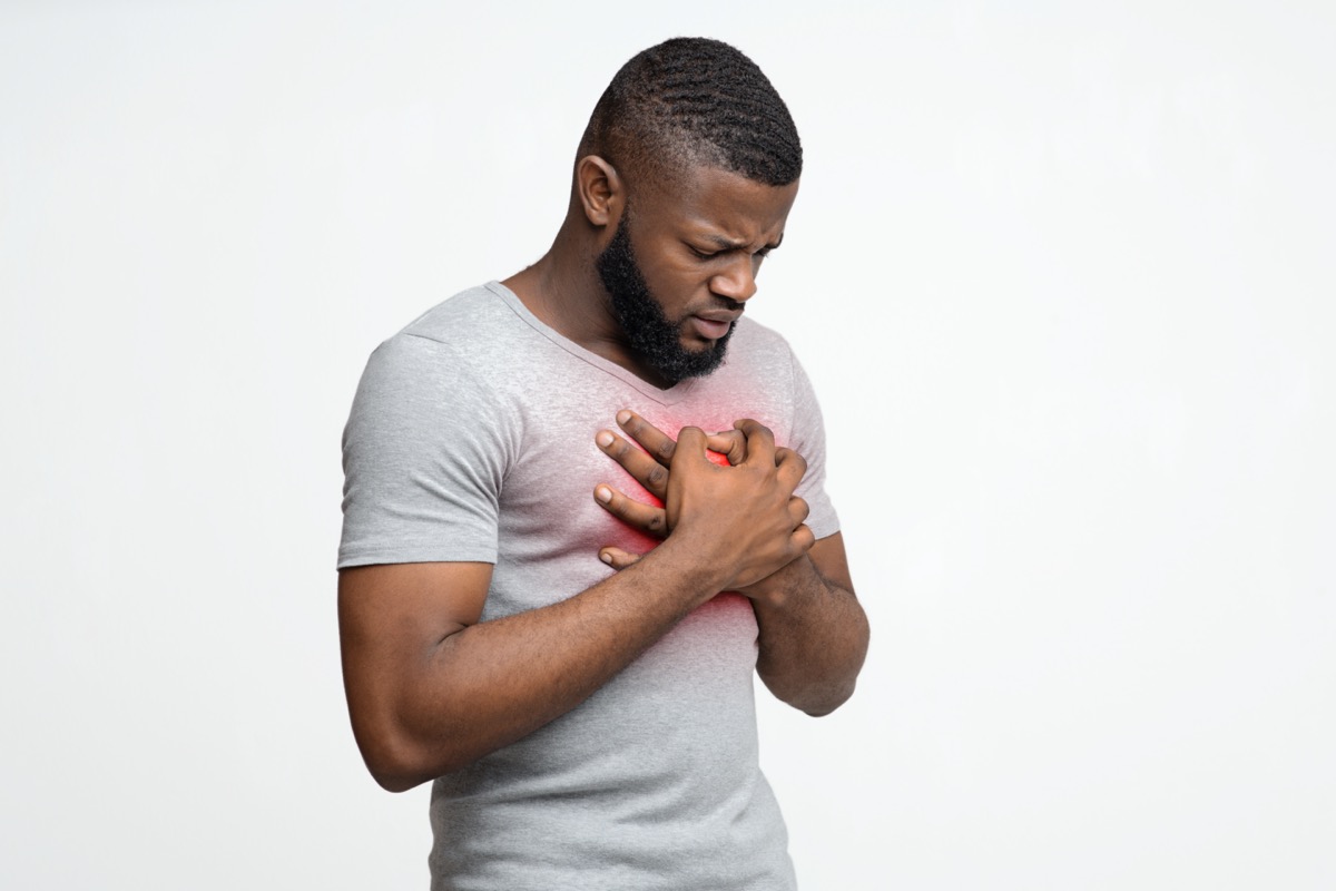 Sad young black man rubbing his chest over white background, free space, heart disease in young age