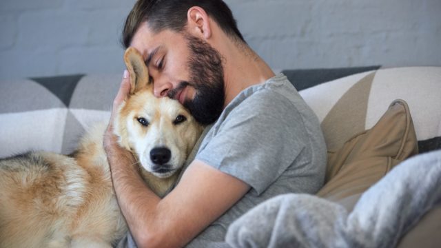 man snuggling and hugging his dog, close friendship loving bond between owner and pet husky