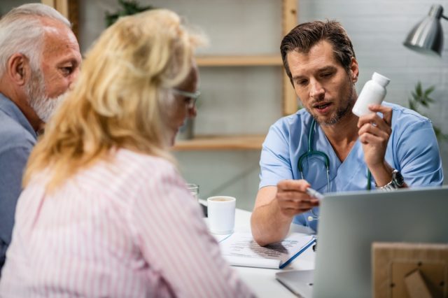 Male doctor advising mature couple about nutritional supplements and using a computer during the appointment.