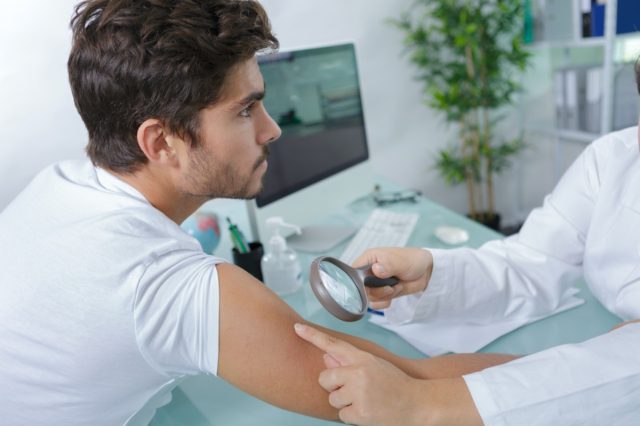 close-up of doctors hands checking mans moles