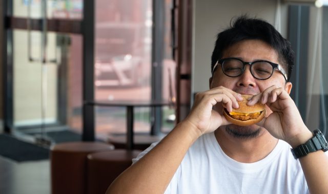 man is eating hamburger in a fast food restaurant and enjoying delicious food