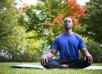 young black man wearing athletic wear sitting in the park exercising yoga
