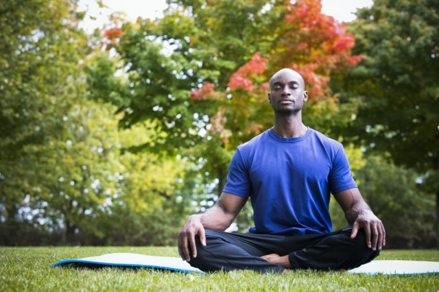 young black man wearing athletic wear sitting in the park exercising yoga