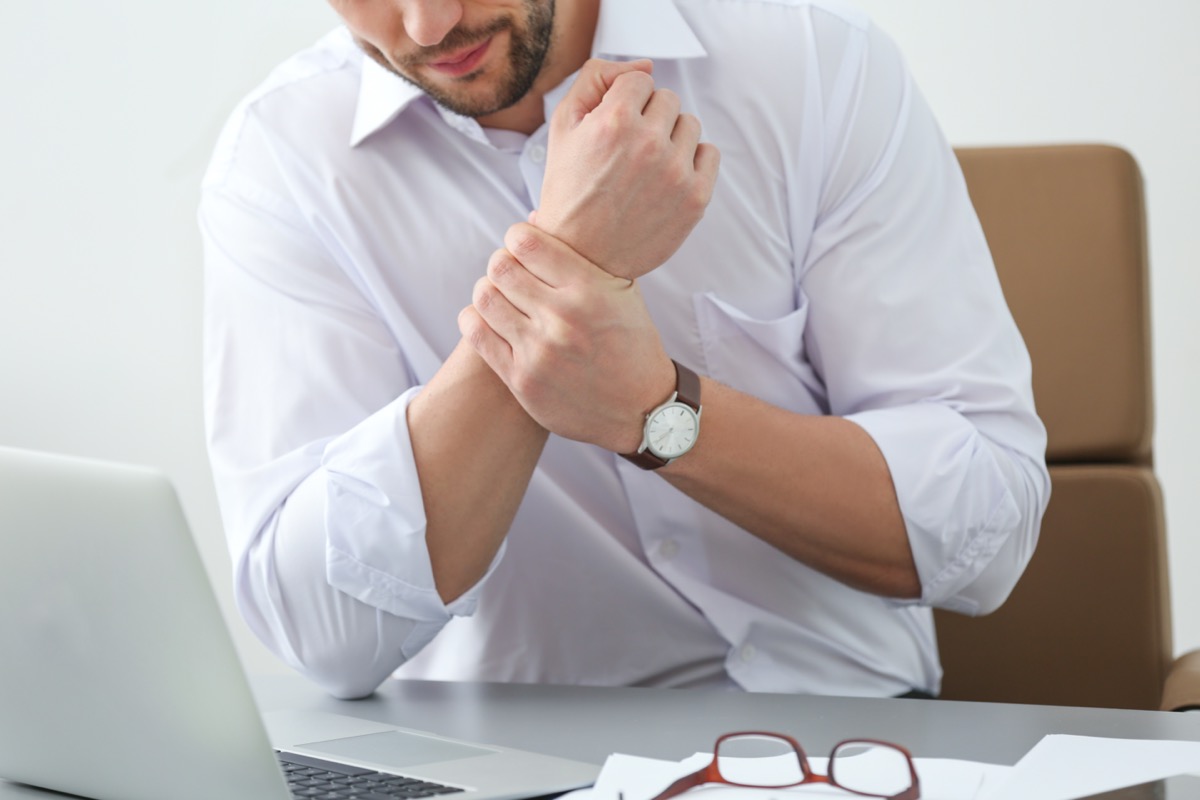 Handsome man suffering from wrist pain in office, closeup