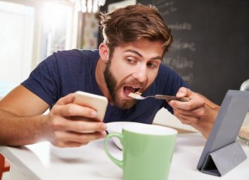 Man Eating Breakfast Whilst Using Digital Tablet And Phone