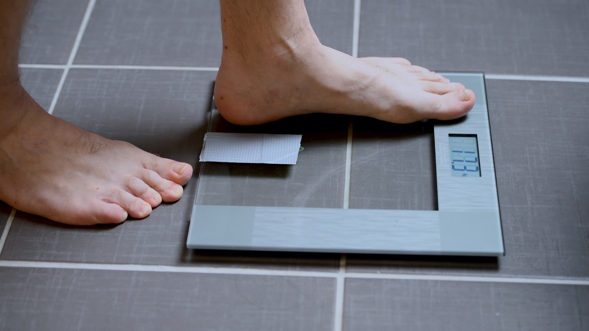 Male feet on glass scales, men's diet, body weight, close up, man stepping up on scales
