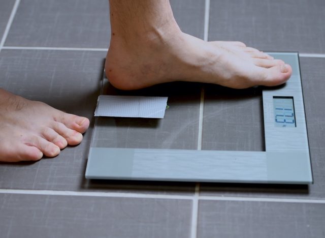 Male feet on glass scales, men's diet, body weight, close up, man stepping up on scales
