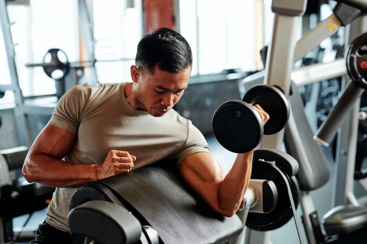 Fit serious Asian athlete by exercising with weights in the gym