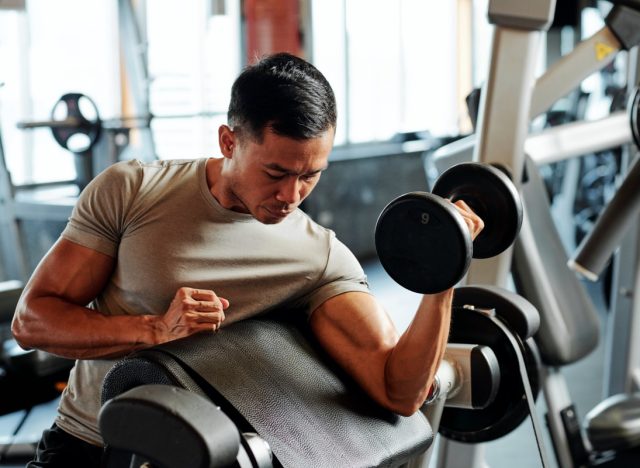 Fit serious Asian sportsman exercising with weights in gym