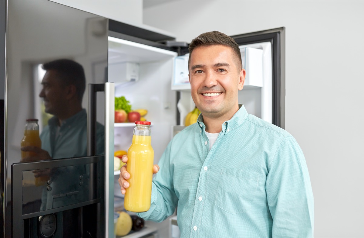 middle-aged man taking bottle of orange juice from fridge at home kitchen