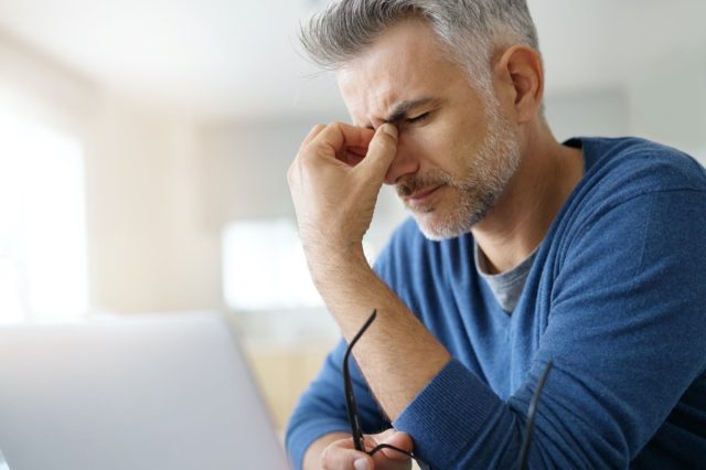 Man at home having headache in front of laptop