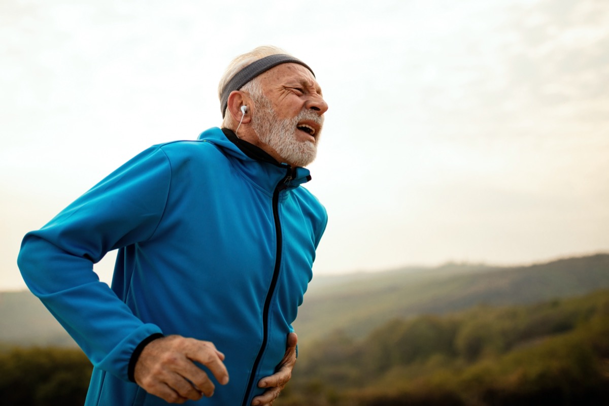 Mature athletic man getting out of breath while feeling pain during morning run in nature.