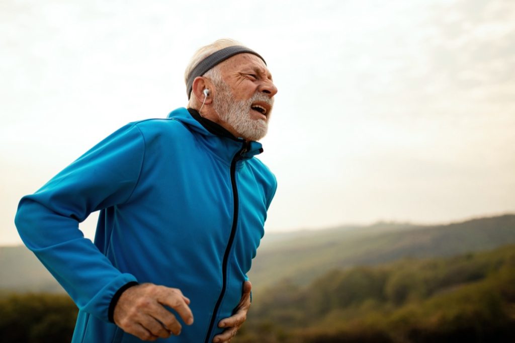 Mature athletic man running out of breath while feeling pain during morning run in nature.