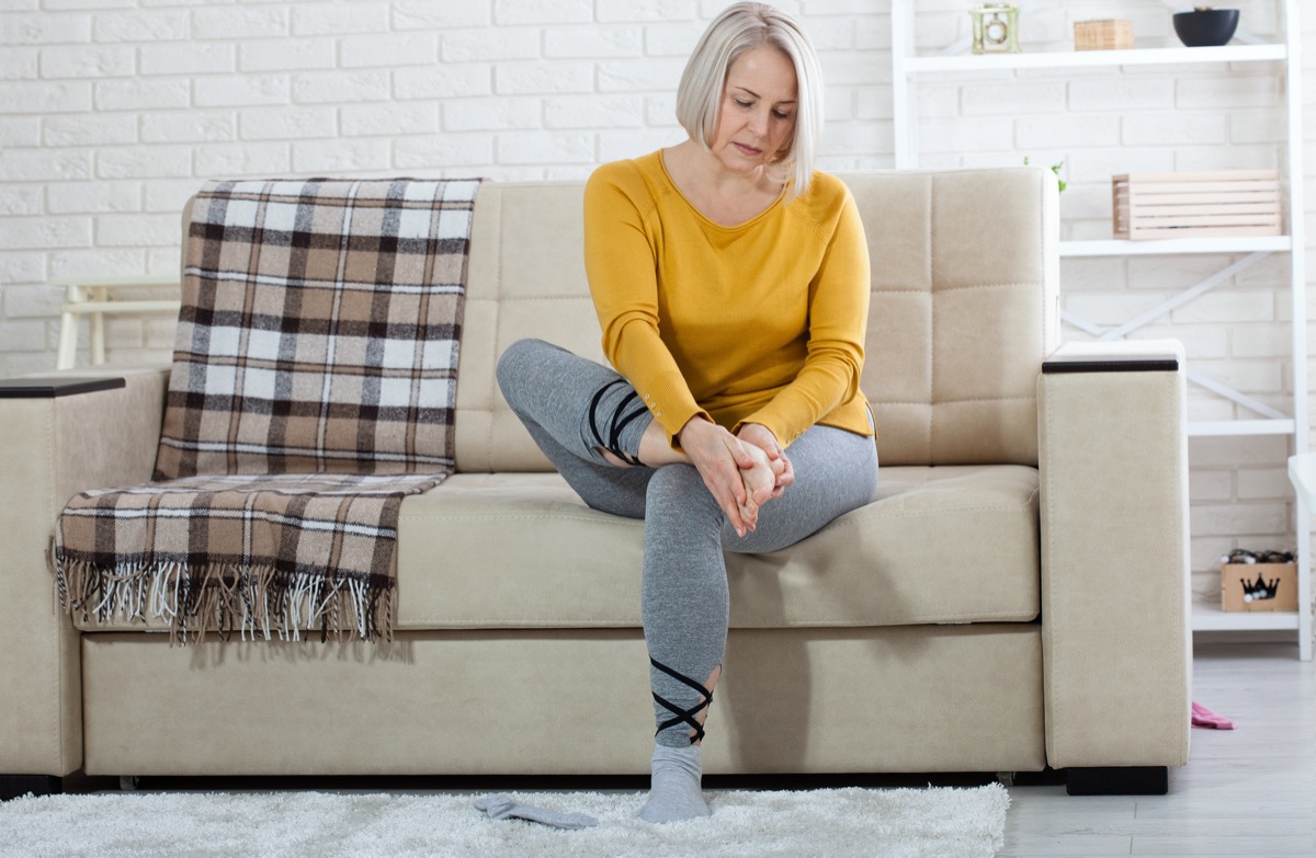 Middle-aged woman suffering from pain in leg at home, closeup