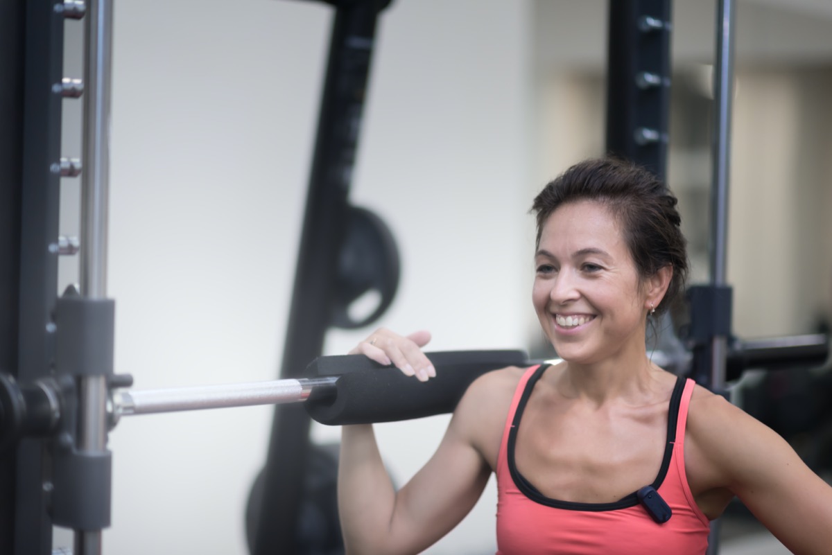 middle age woman in red shirt is standing in the gym near the rod