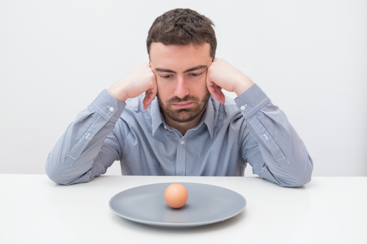 Hungry man feeling sad in front of a dish with an egg