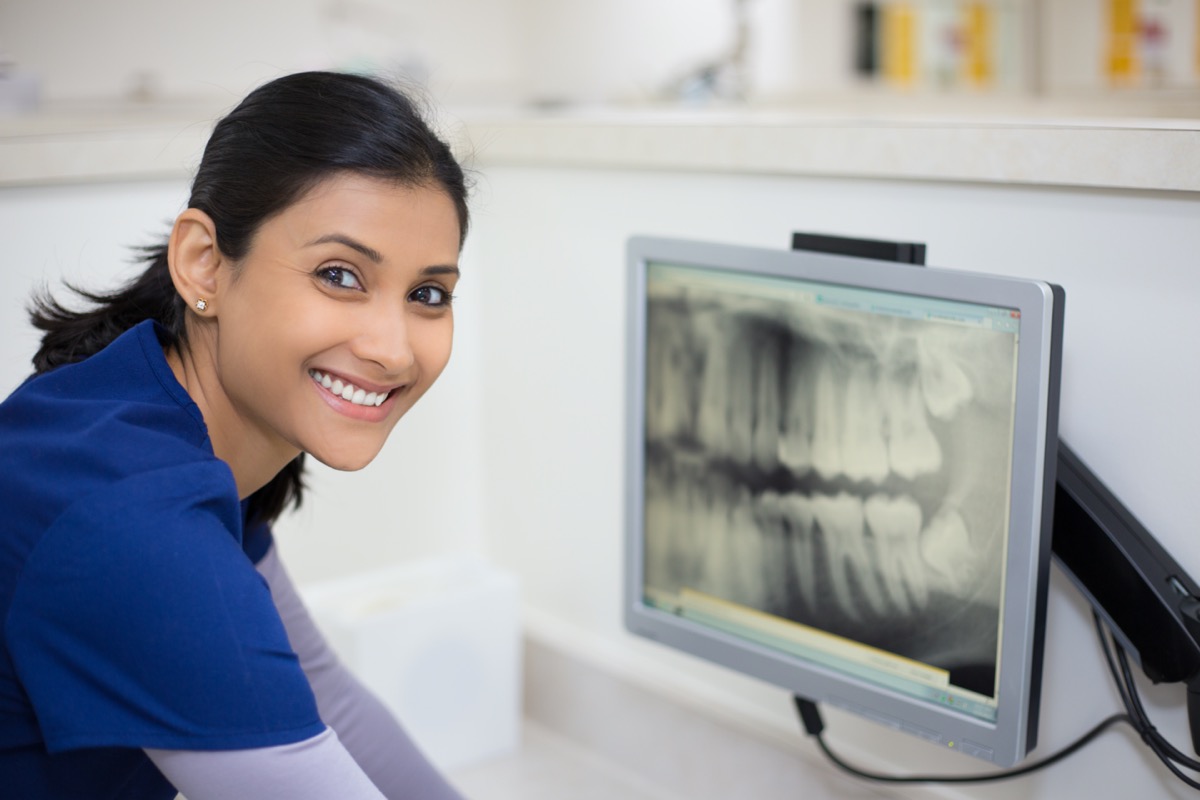 Closeup portrait of allied health dental professional in blue scrubs examining dental x-ray on computer screen, isolated dentist office